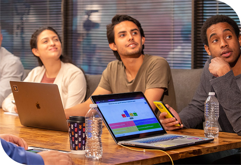 A diverse group of professionals collaborates around a table, each using laptops for engaging training activities.