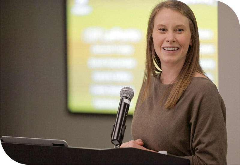 A woman presents at a podium, showcasing engaging training methods for corporate development and employee engagement.